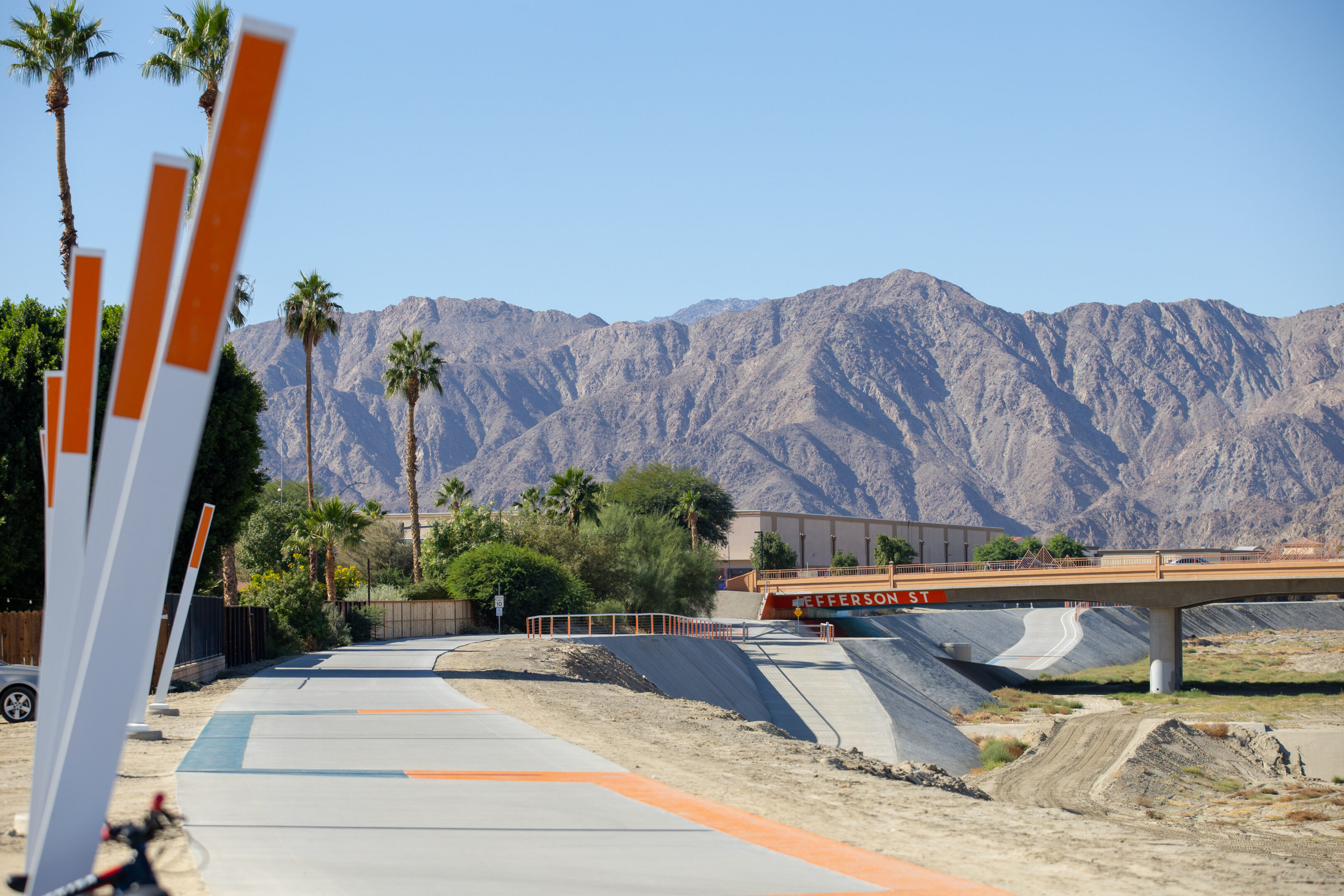 A dry riverbed with mountains and palm trees in the background.