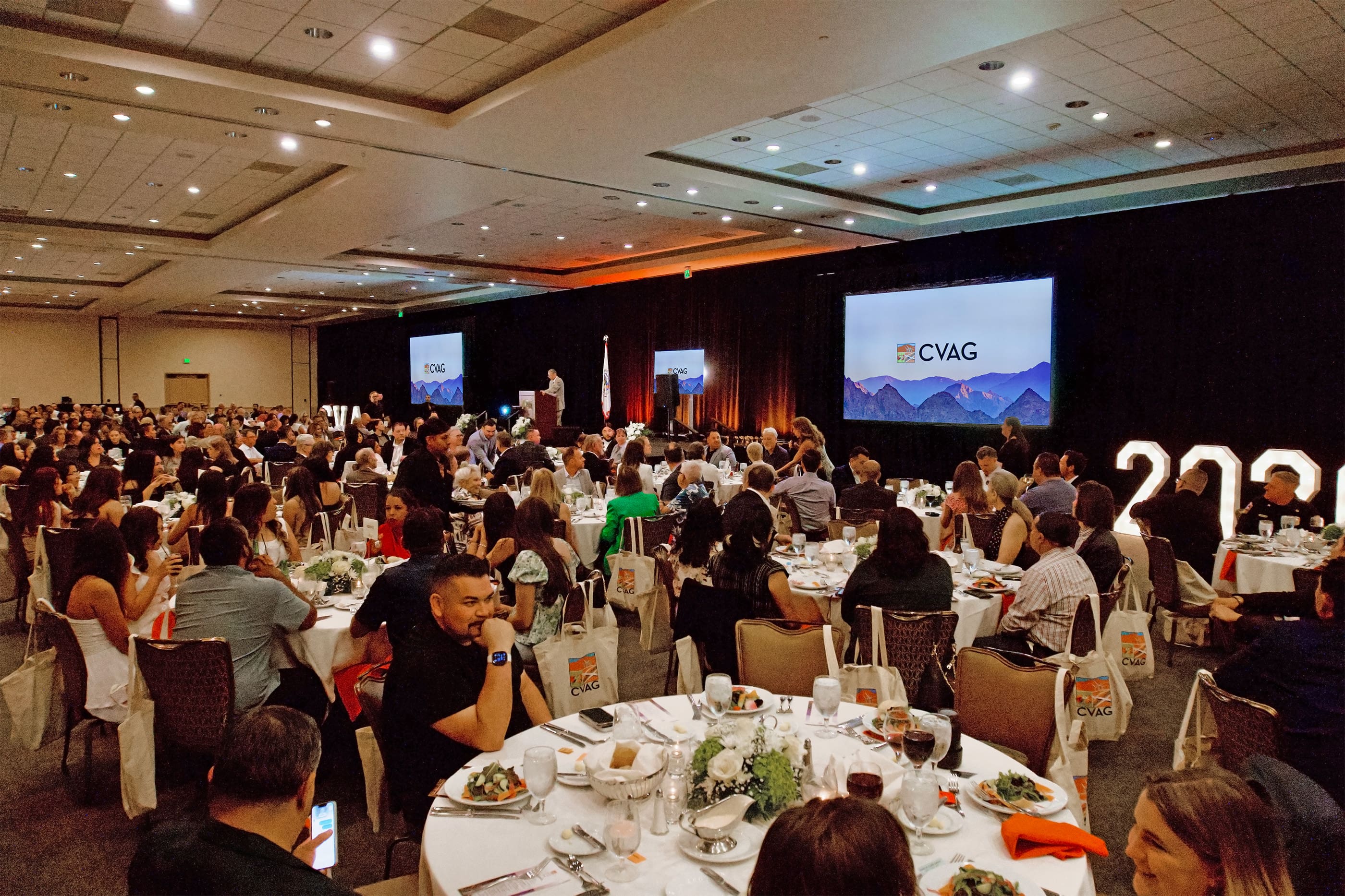 Crowded banquet hall with stage and screens